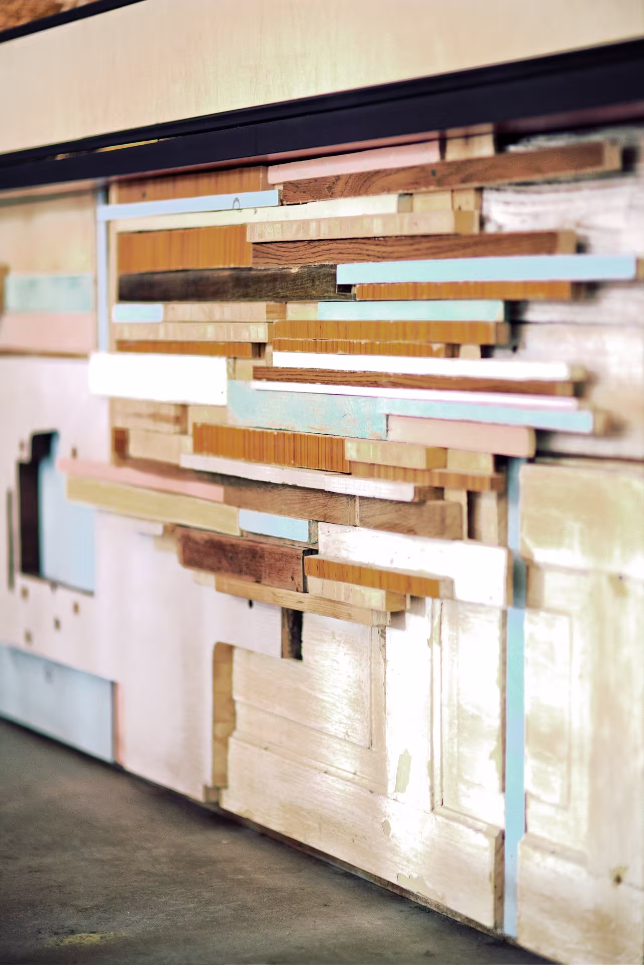 A close-up view of a wall art installation made from layered, painted, and unpainted wooden planks arranged in a geometric pattern.