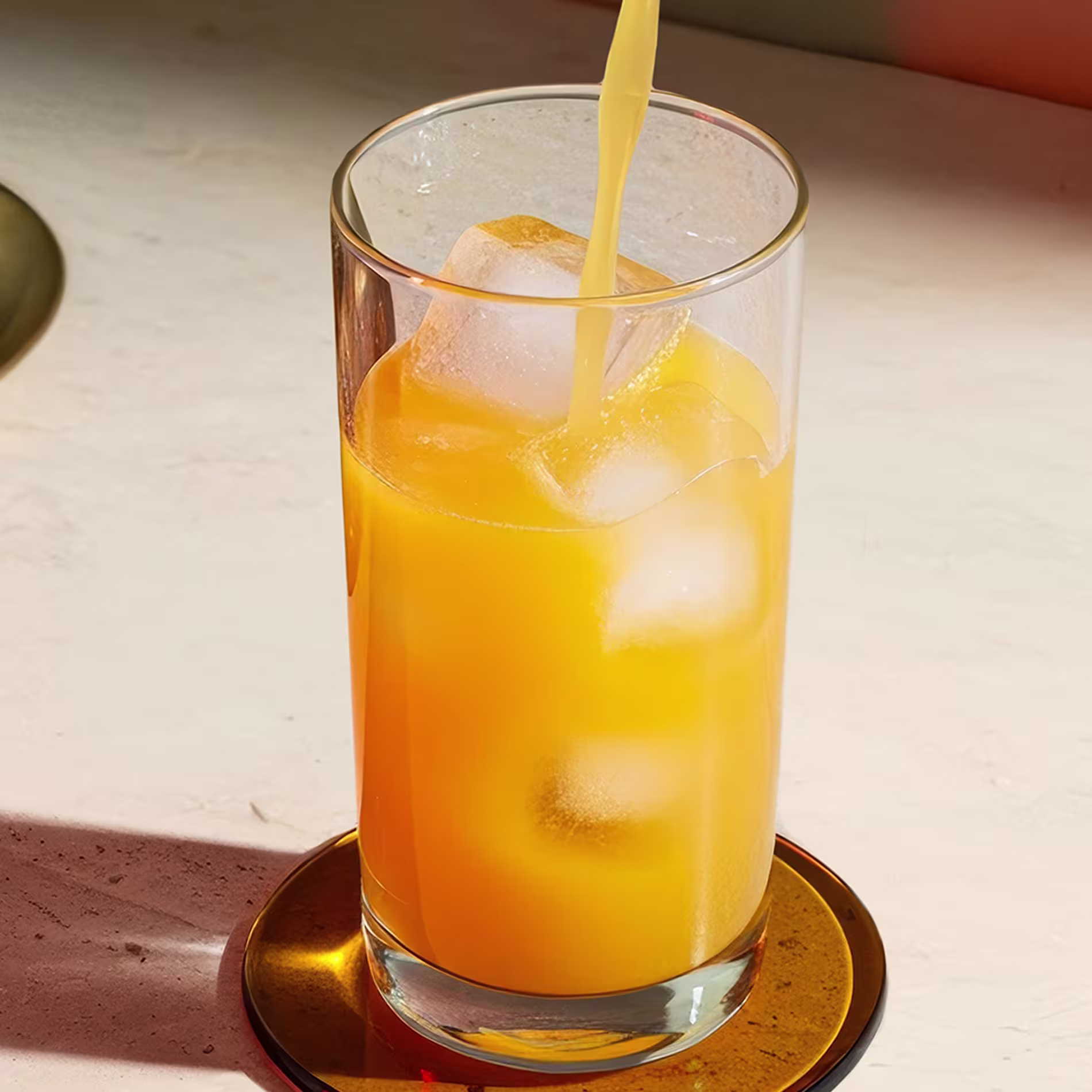 Orange juice being poured into a Collins glass.