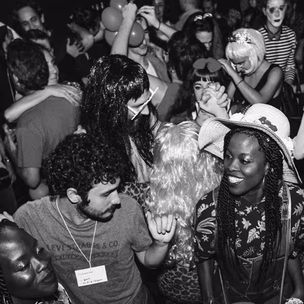 La foto muestra un evento social en un espacio interior lleno de gente en la Sala Upload