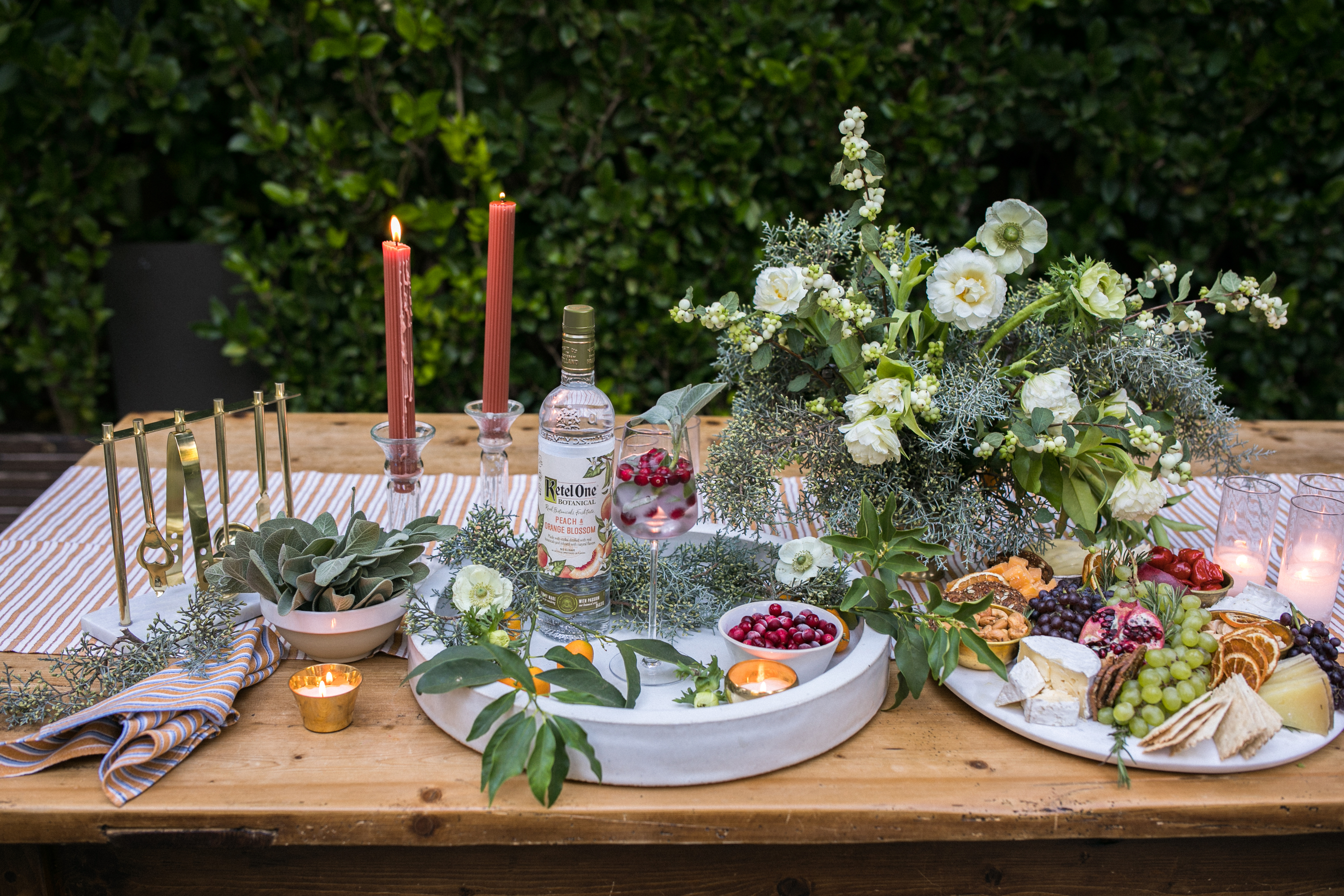 A picture of a set table scape, complete with candles, flowers, plates of food and a bottle of Ketel One vodka