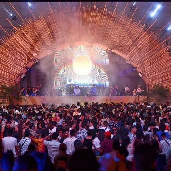 La imagen muestra un grupo de gente mirando hacia el escenario de La Huaka.