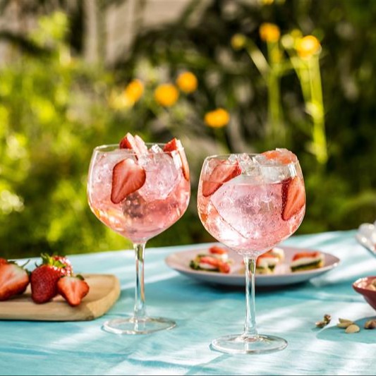 Gordon's pink gin and tonic cocktails with ice and fresh strawberry slices served outdoors on a sunny day