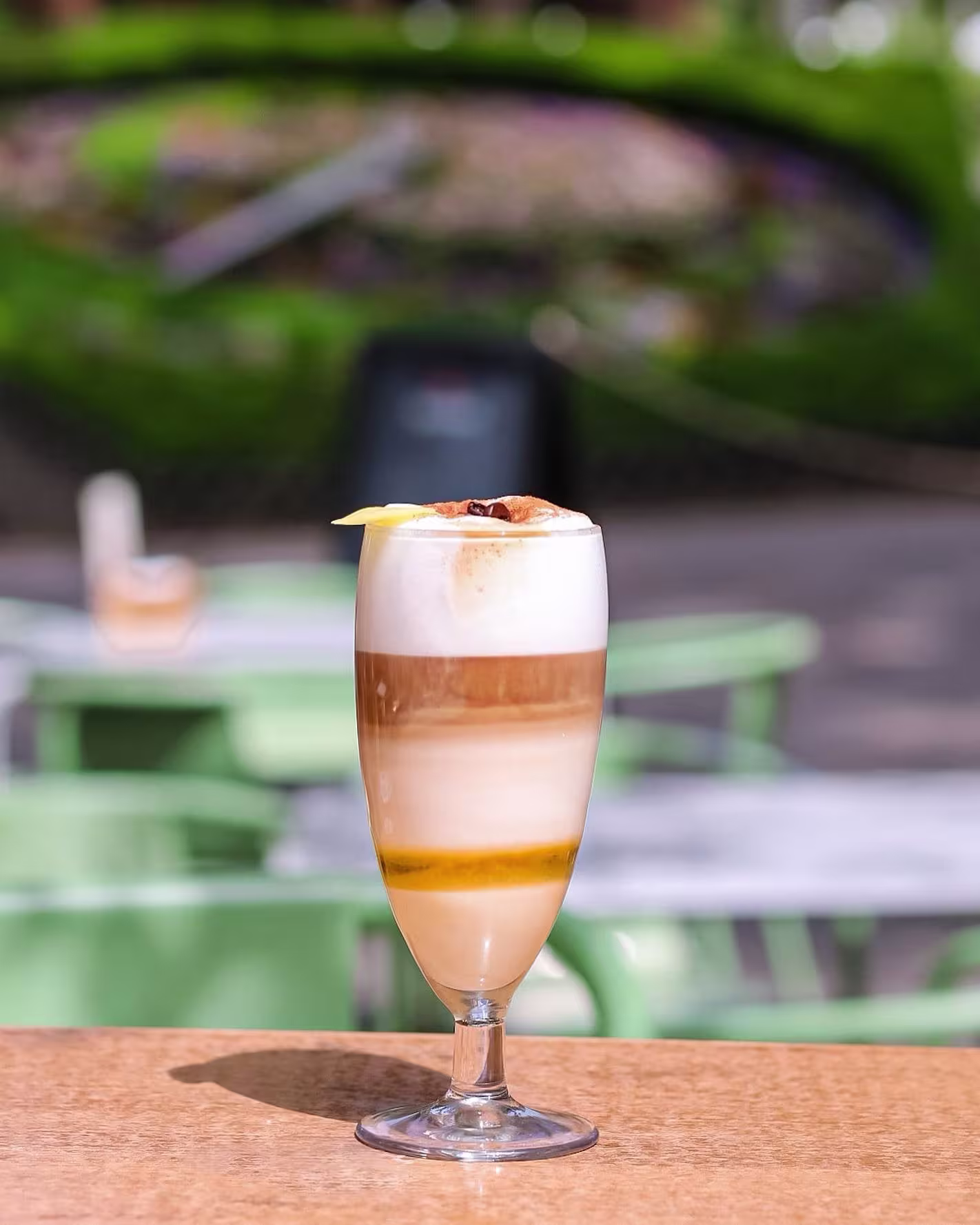Cóctel en Terraza Parque con capas de crema y café, decorado con piña y granos de café. Ambiente soleado y relajado al aire libre.