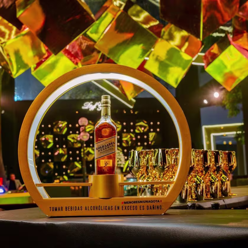 La imagen muestra la botella del whisky Johnnie Walker Gold Label Reserve y copas doradas al costado sobre una barra.