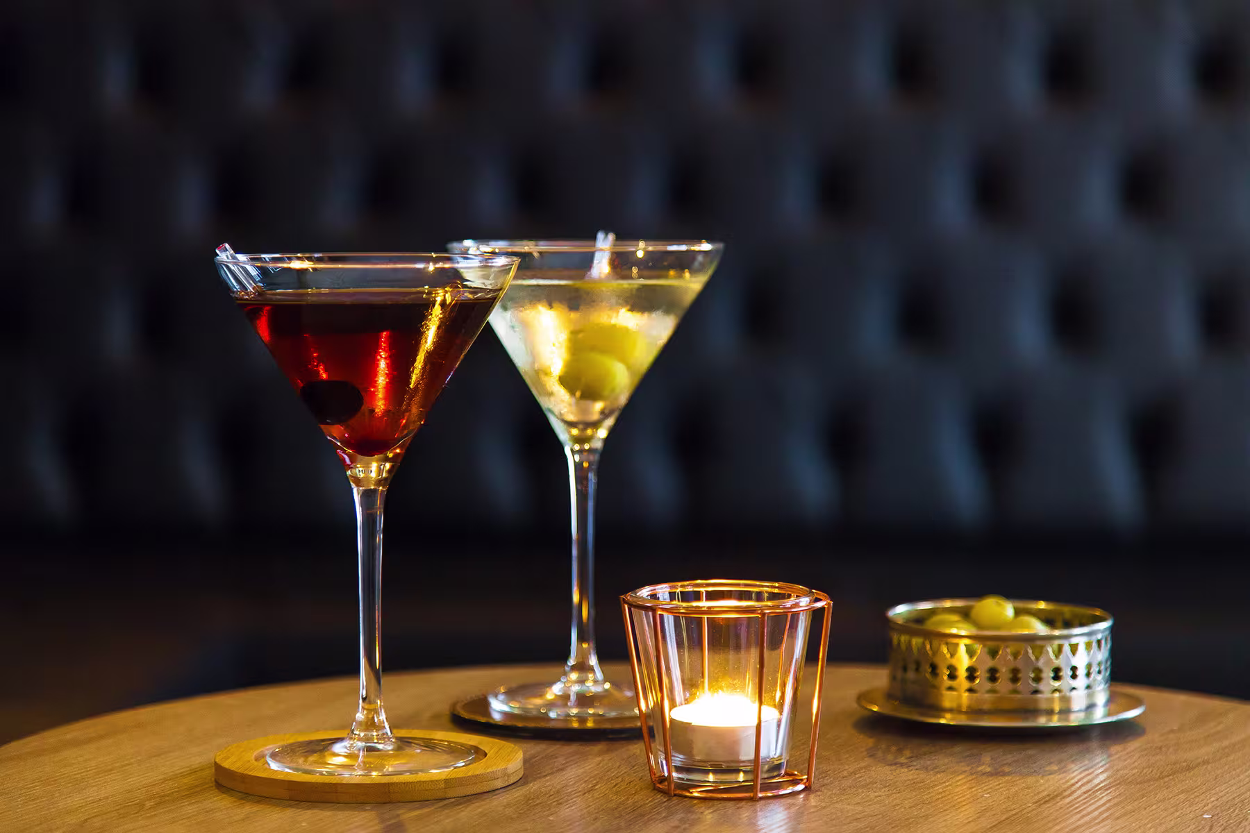 Mesa en La Mula de Moscú con dos cócteles en copas de Martini, vela decorativa y aceitunas en un cuenco metálico.