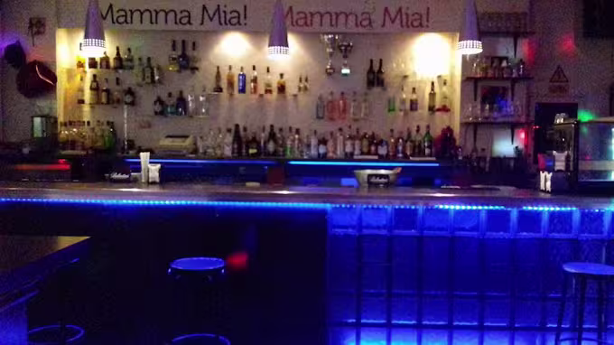 Barra iluminada de Peter's Bar con luces azules, botellas ordenadas y lámparas colgantes. Ambiente moderno y acogedor.