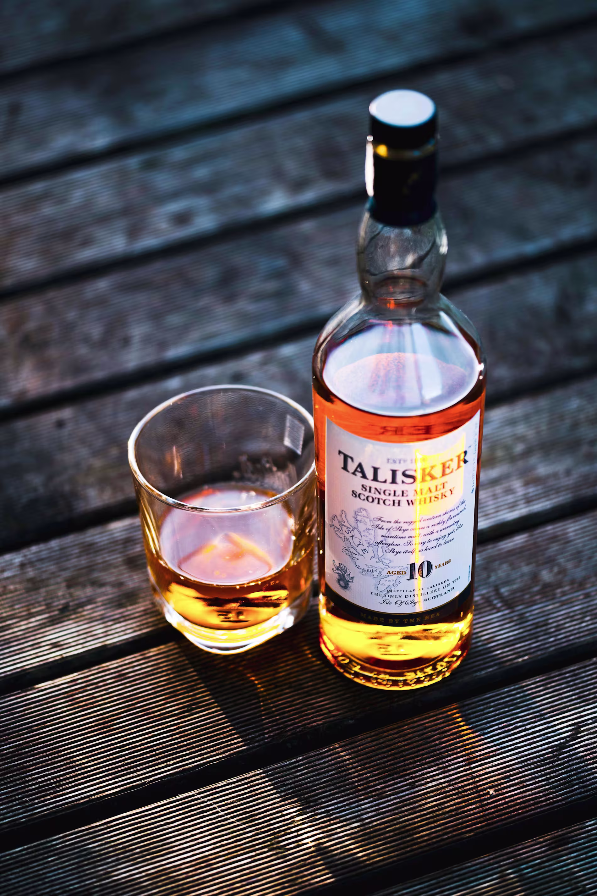 A bottle of Talisker 10-year-old single malt Scotch whisky and a glass with whisky sit on a wooden surface.