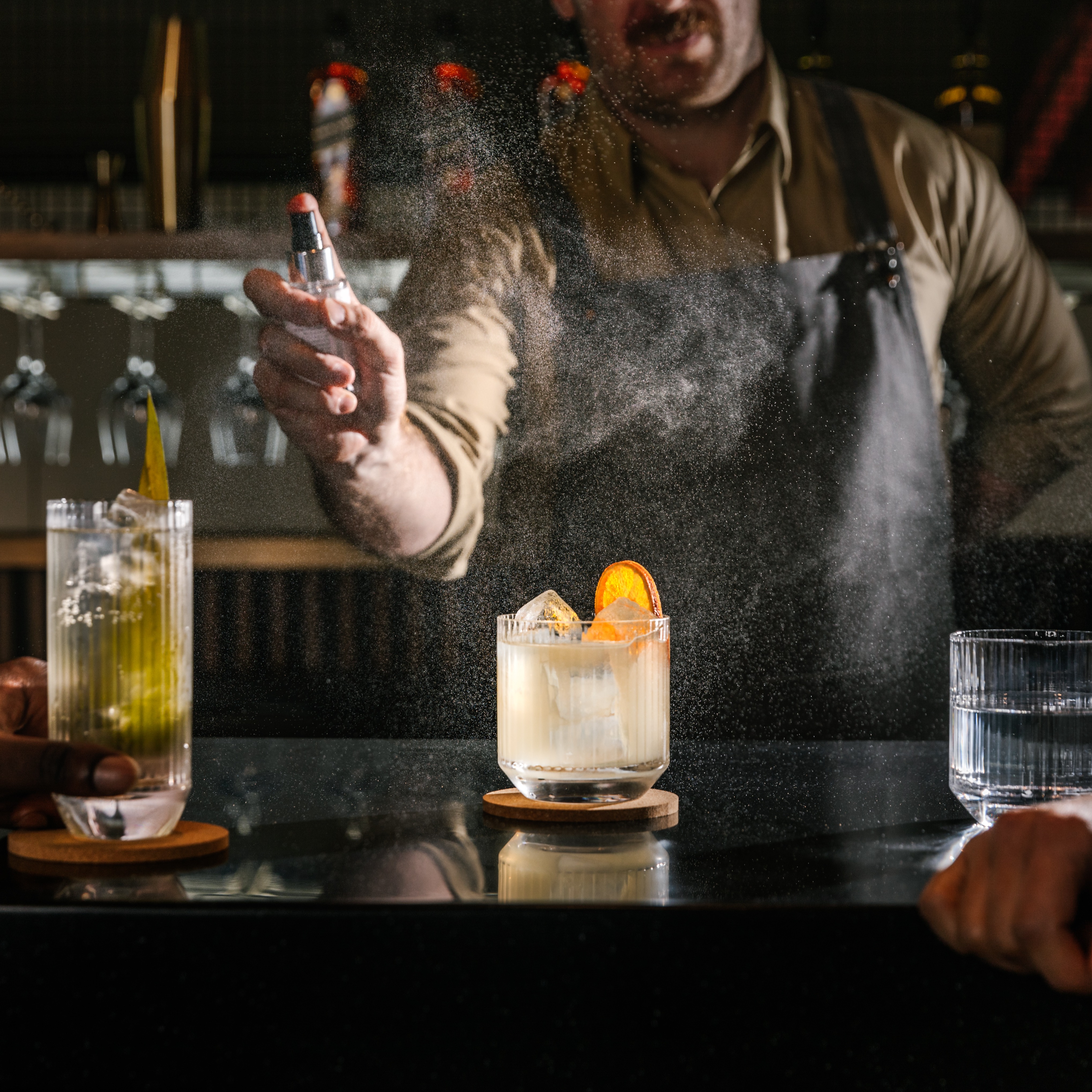 A bartender sprays a cocktail on a dark bar. 