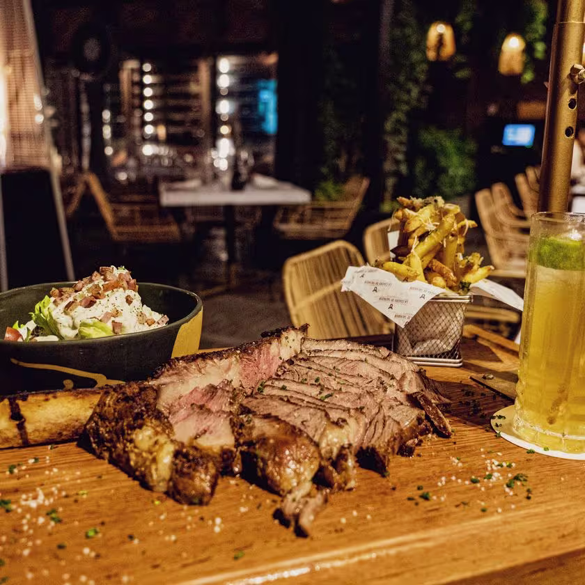 Foto del plato completo. El Tomahawk rebanado y acompañado de una ensalada Wedge y papas trufadas. El Black Highwall, un refrescante cóctel hecho con Johnnie Walker Black Label completa el plato como maridaje perfecto.