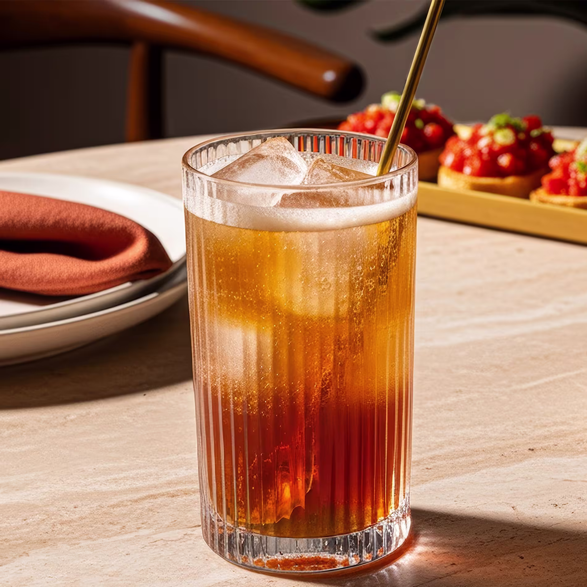 A metal spoon stirring a Dark and Stormy cocktail in a highball glass.