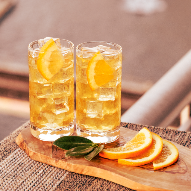 Two tall cocktails with orange garnishes on a wooden board, covered with orange slices.