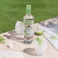 La imagen muestra una botella de vodka Smirnoff Green Apple y dos vasos rellenos con el cóctel Mojito con Vodka Smirnoff Green Apple.