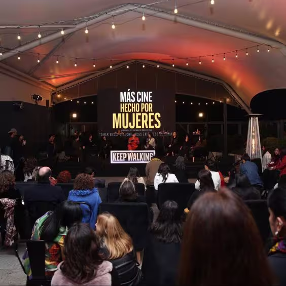 La imagen muestra un foto panorámica del conversatorio y, de fondo, una pantalla con el texto: Más cine hecho por mujeres.
