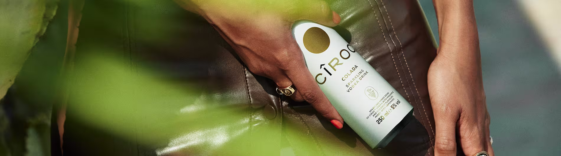 Hand holding a Cîroc Colada ready-to-drink cocktail can, partially hidden by leave