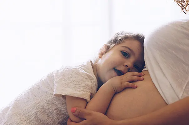 Kleinkind horcht am Bauch der schwangeren Mutter