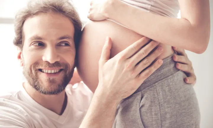 Mann umarmt den Bauch seiner schwangeren Partnerin