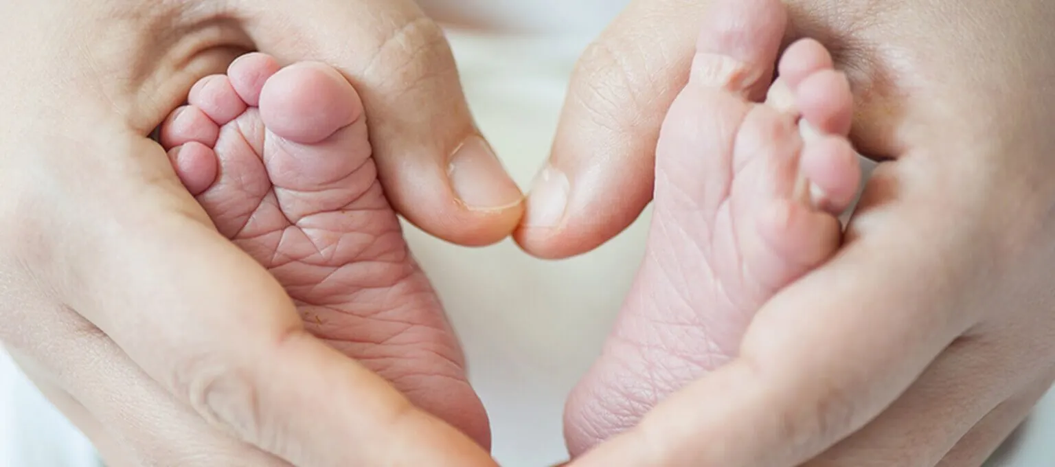 Hände halten Babyfüße in Form eines Herzens