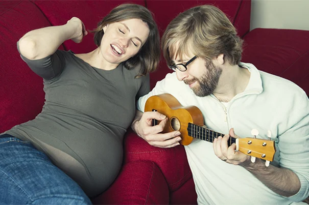 Ein Mann spielt Ukulele neben seiner schwangeren Frau und freut sich auf das Vater werden