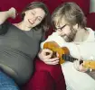 Ein Mann spielt Ukulele neben seiner schwangeren Frau und freut sich auf das Vater werden