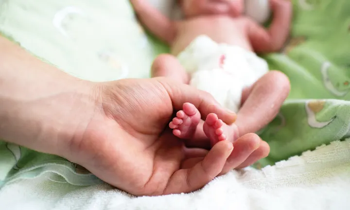 Hände halten die Füßchen eines frühgeborenen Babys