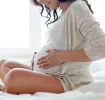 Frau auf Bett umfasst Ihren Schwangerschaftsbauch