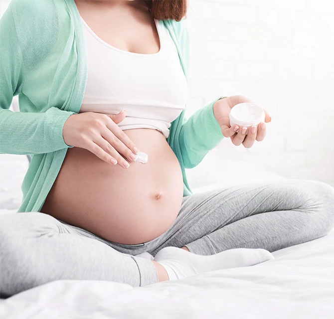 Schwangere Frau cremt Ihren juckenden Bauch ein 