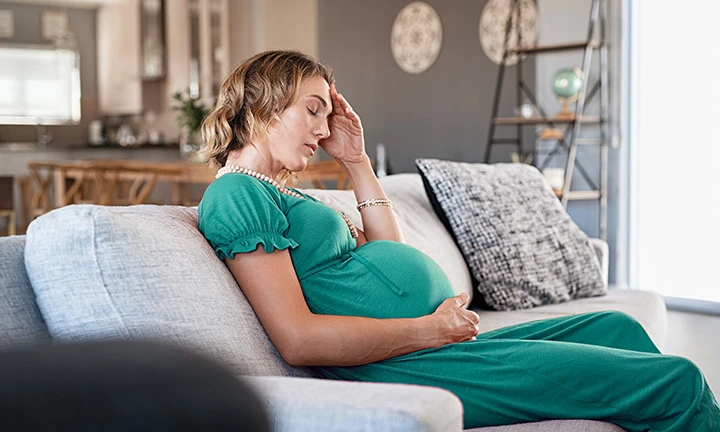 Schwangere Frau mit Eisenmangel sitzt auf Couch 