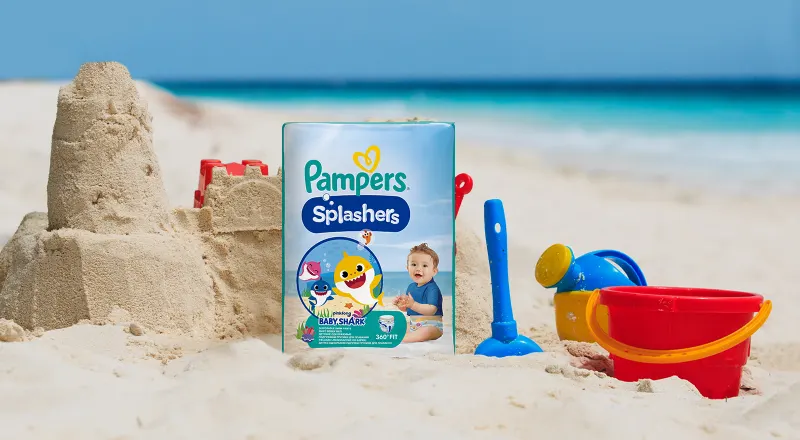 Packung Pampers Splashers am Strand mit Sandburg und Strandspielzeug