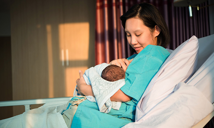Mutter im Wochenbett hält ihr Neugeborenes im Arm