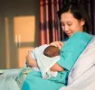Mutter im Wochenbett hält ihr Neugeborenes im Arm