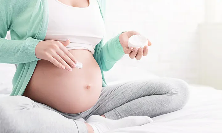 Schwangere Frau cremt Ihren juckenden Bauch ein 