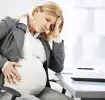 Schwangere Frau mit Schwangerschaftsproblemen sitzt am Schreibtisch