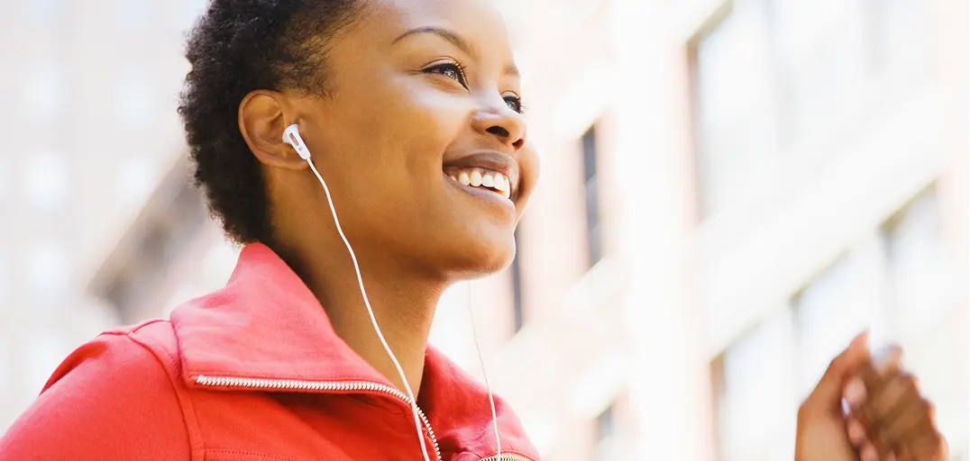Woman jogging in a red jacket with earphones in an urban setting