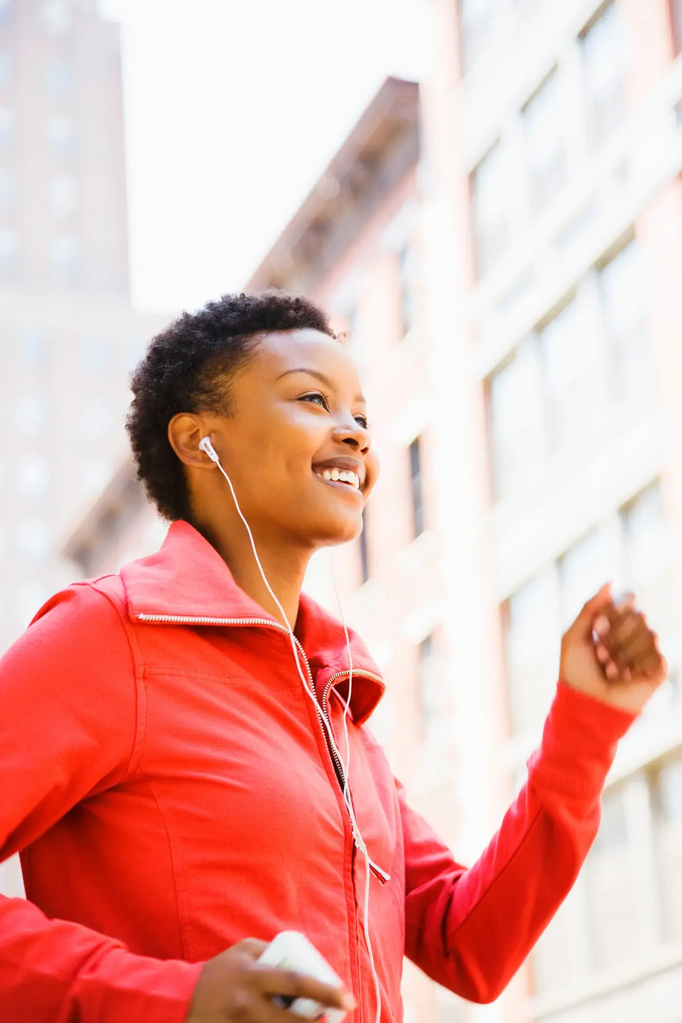 Woman jogging in a red jacket with earphones in an urban setting