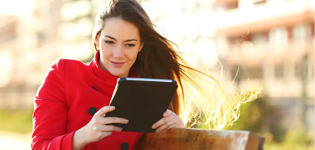 Woman in a red coat reading a tablet outdoors on a sunny day