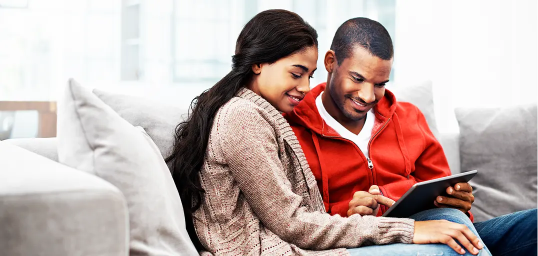 Couple sitting on a couch together, sharing a tablet in a cozy living room