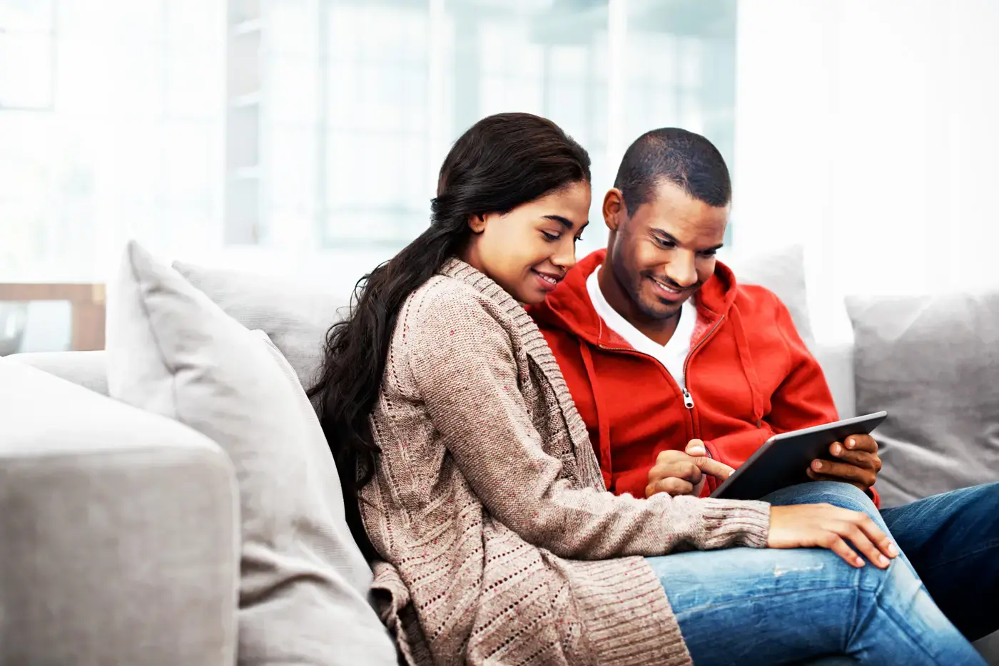 Couple sitting on a couch together, sharing a tablet in a cozy living room