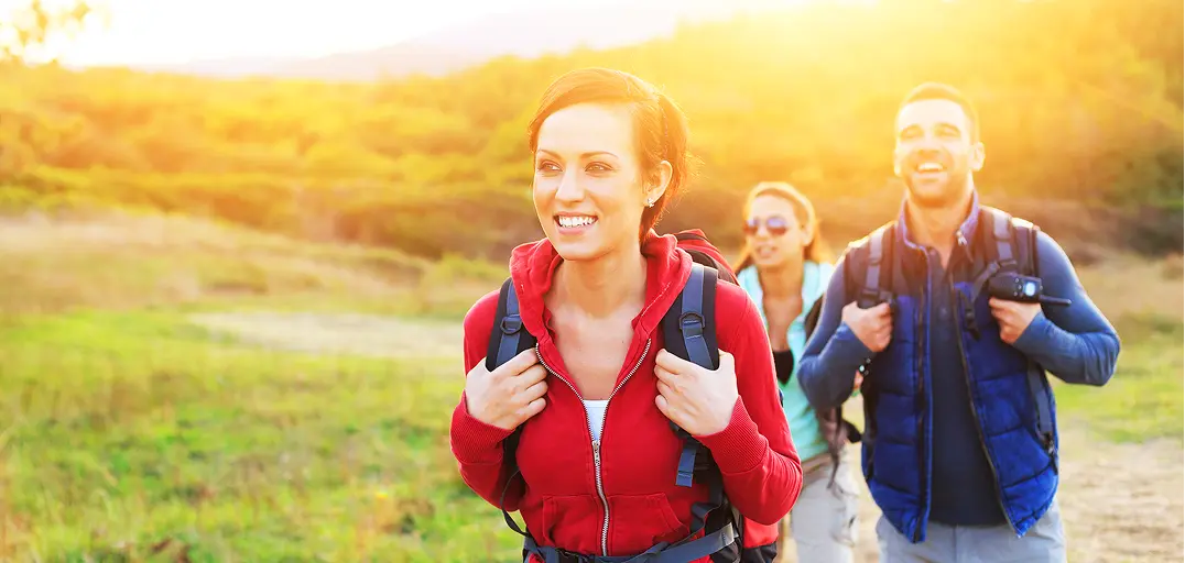 Group of 3 hikers with backpacks walking on a trail during sunset