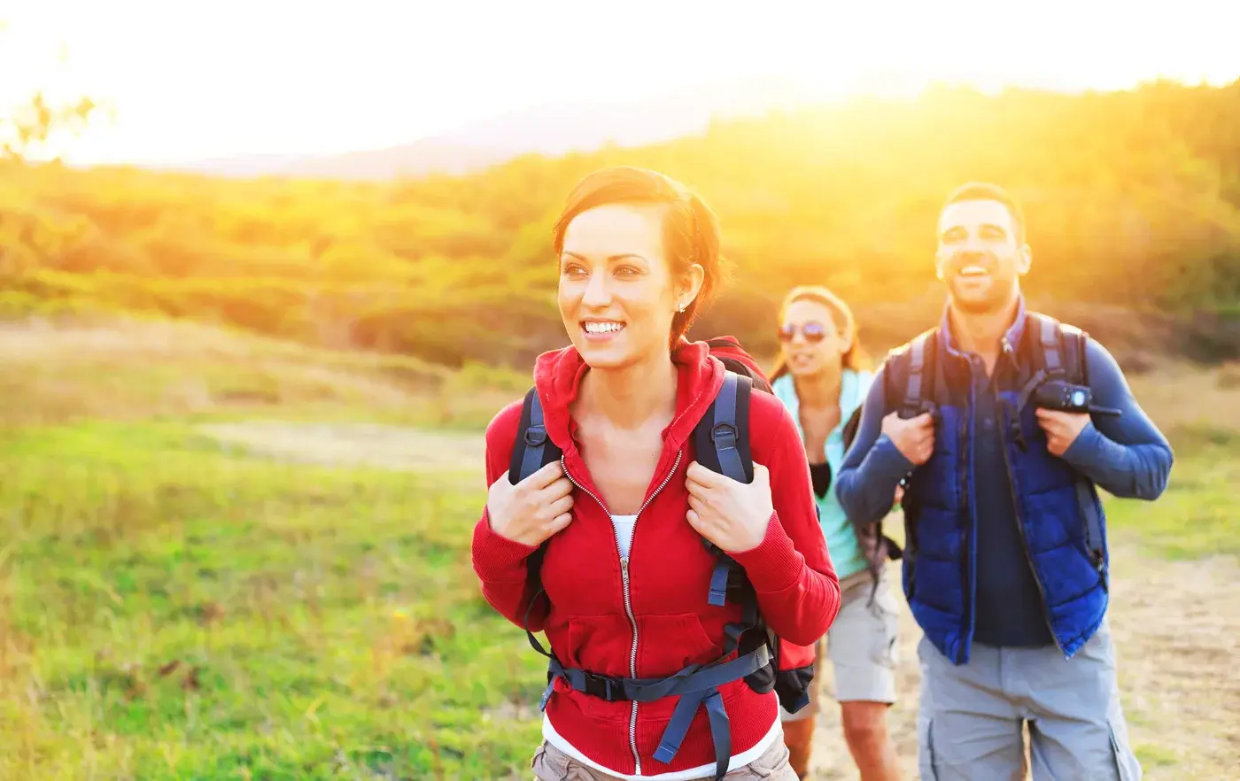 Group of 3 hikers with backpacks walking on a trail during sunset