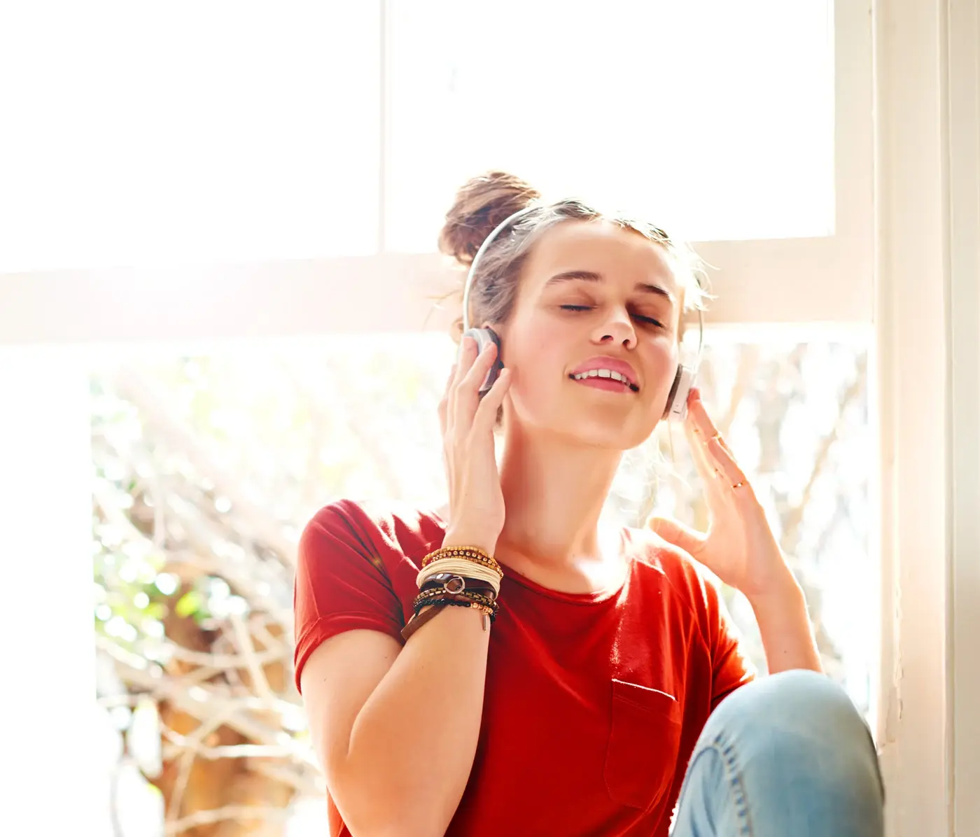 Woman wearing headphones near a sunlit window