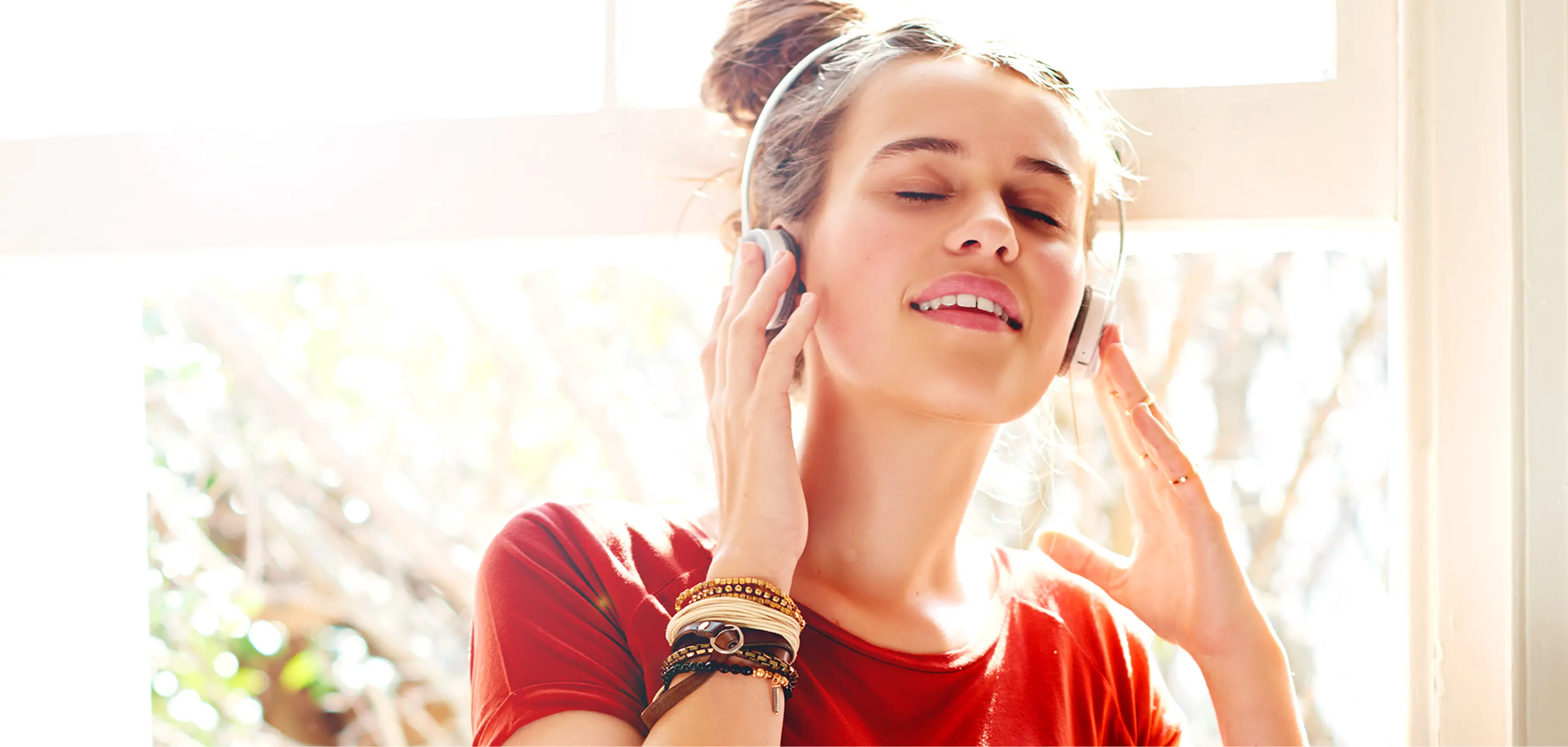Woman wearing headphones near a sunlit window
