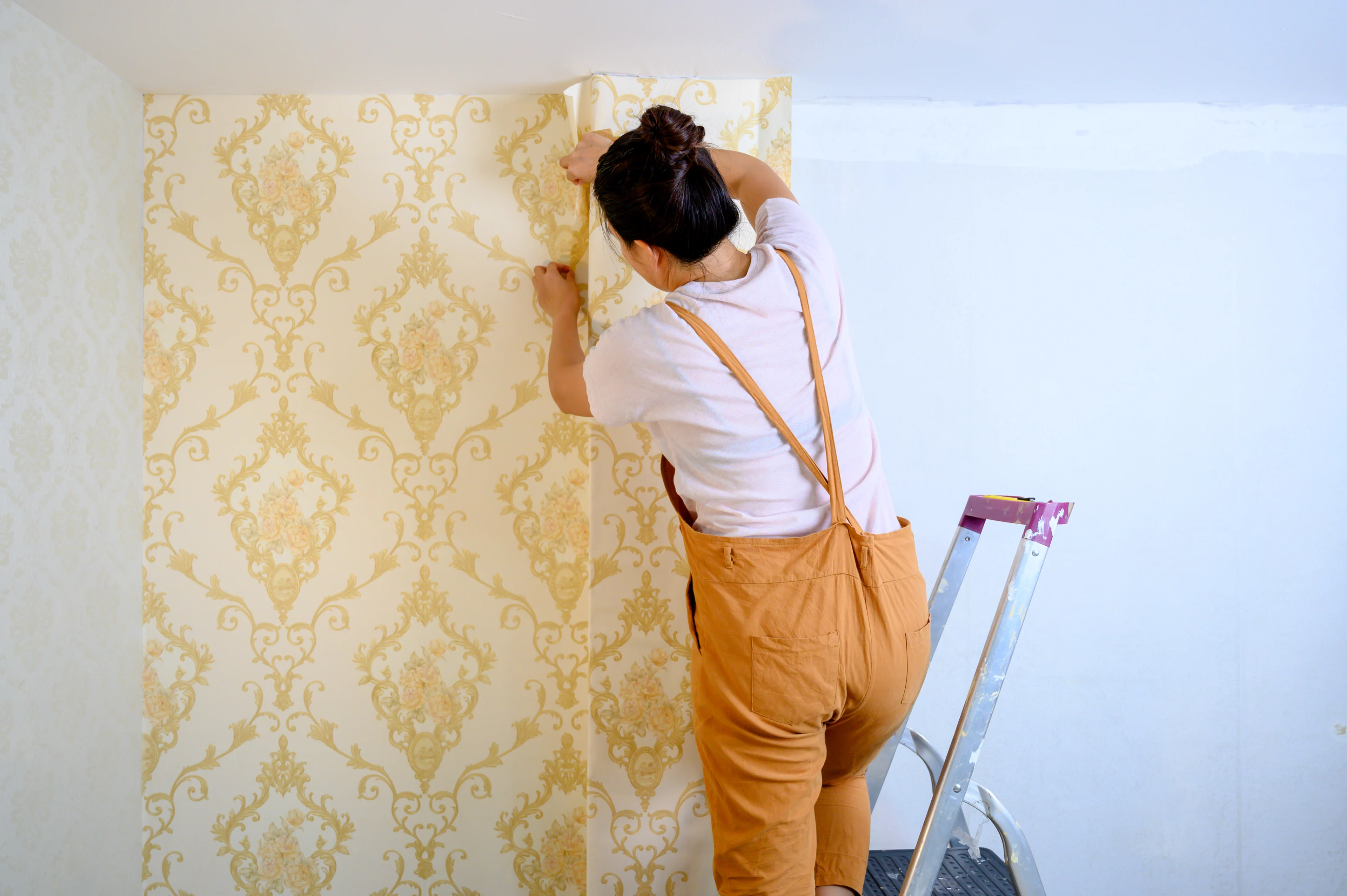 a woman hanging wallpaper with a yellow design on it. 