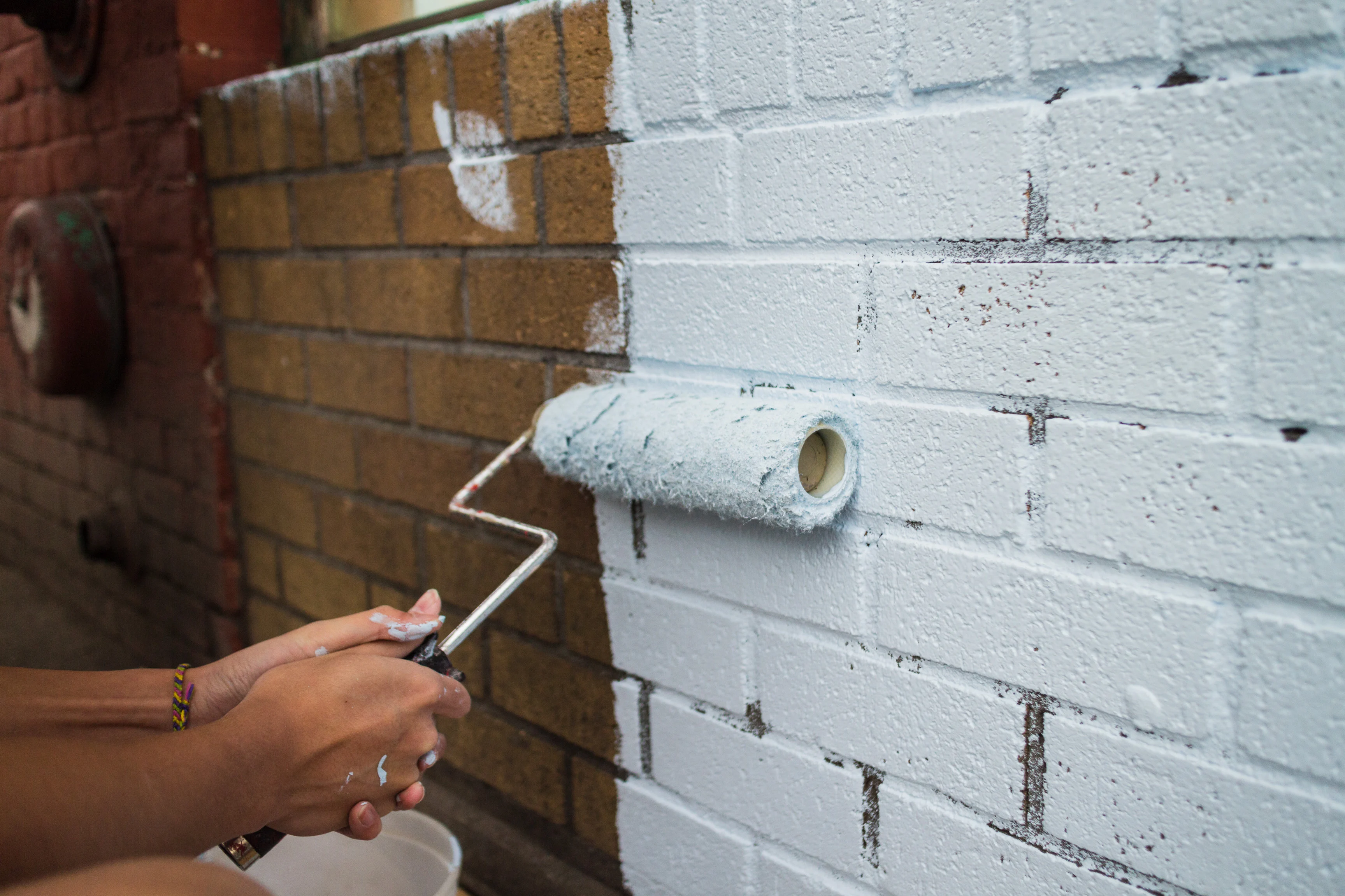 a person painting a brick wall white with a paint roller