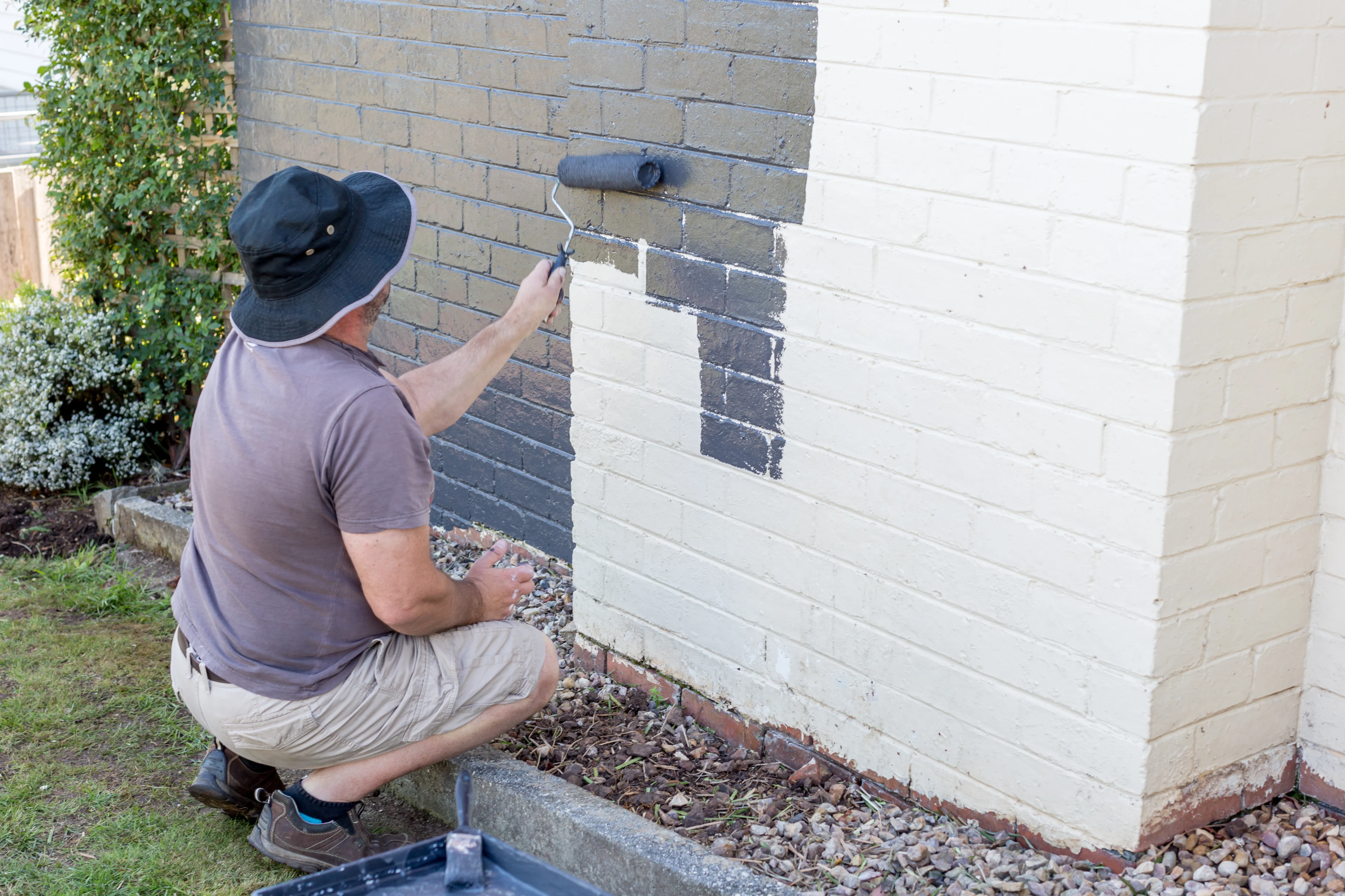 a person painting an exterior brick wall grey using a paint roller
