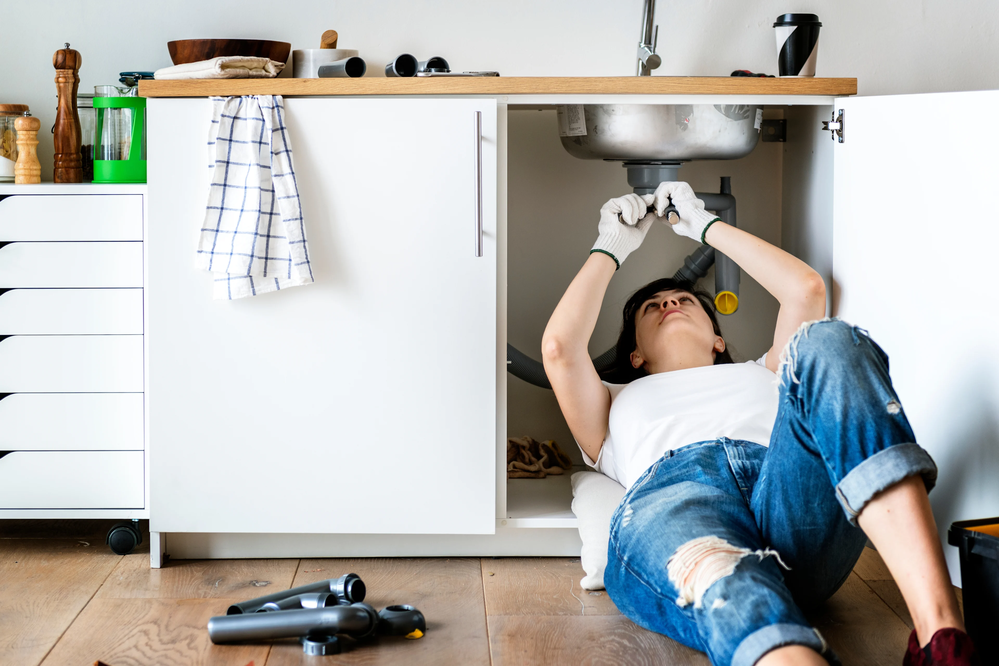 someone using a spanner to tighten a drain pipe underneath a sink. 