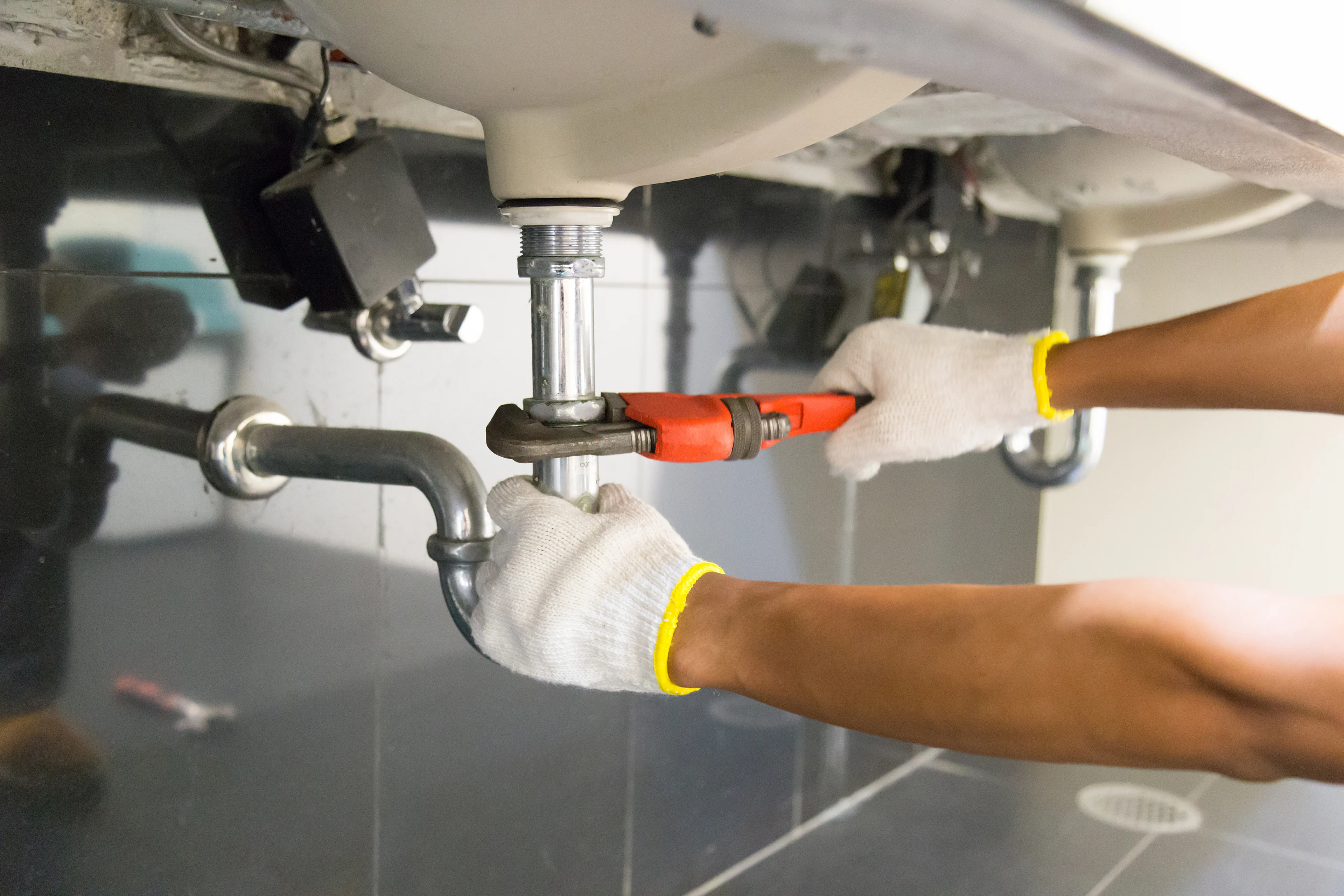 someone using a monkey wrench to tighten a drain pipe underneath a sink. 