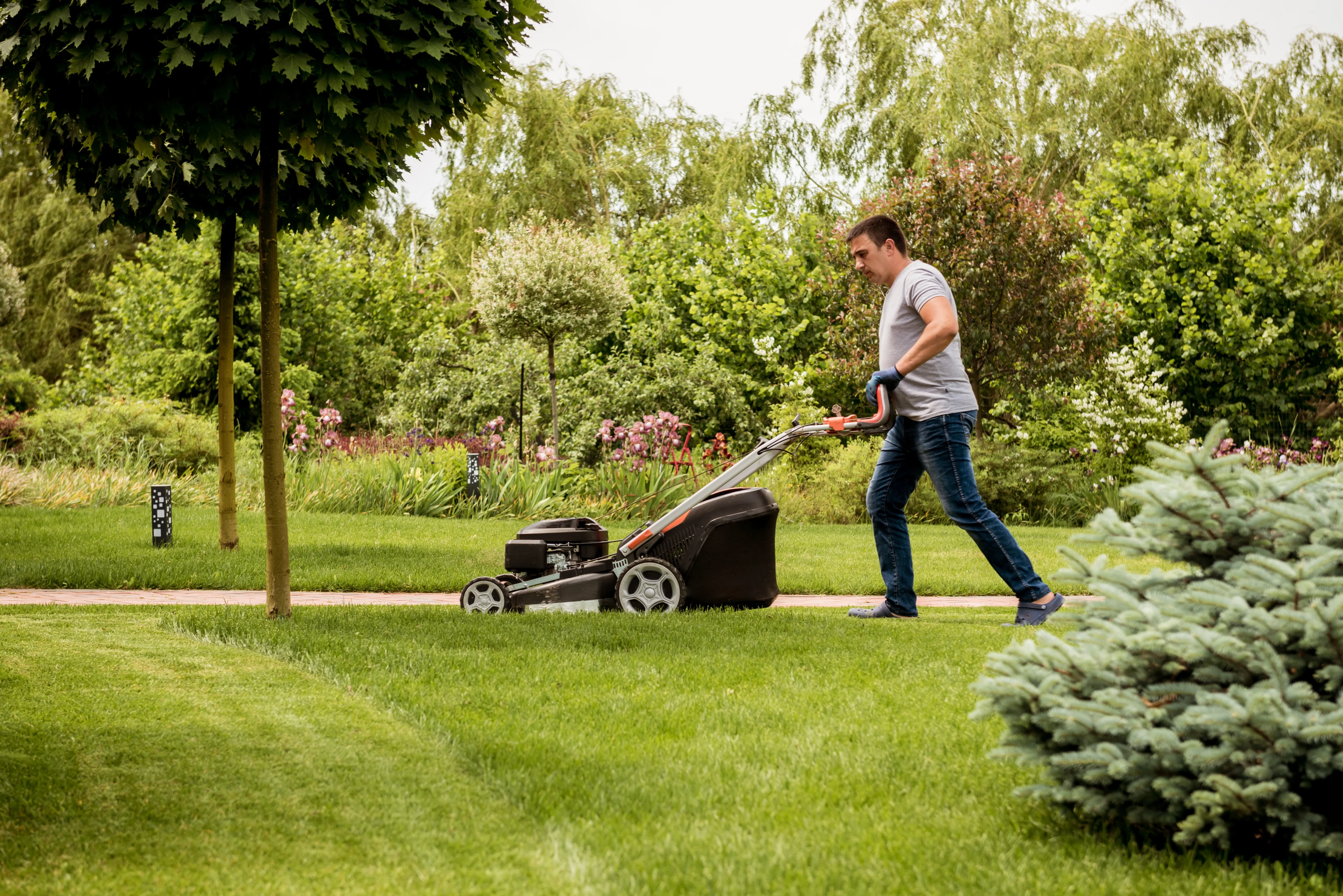 a man mowing a lawn with a lawnmower. 