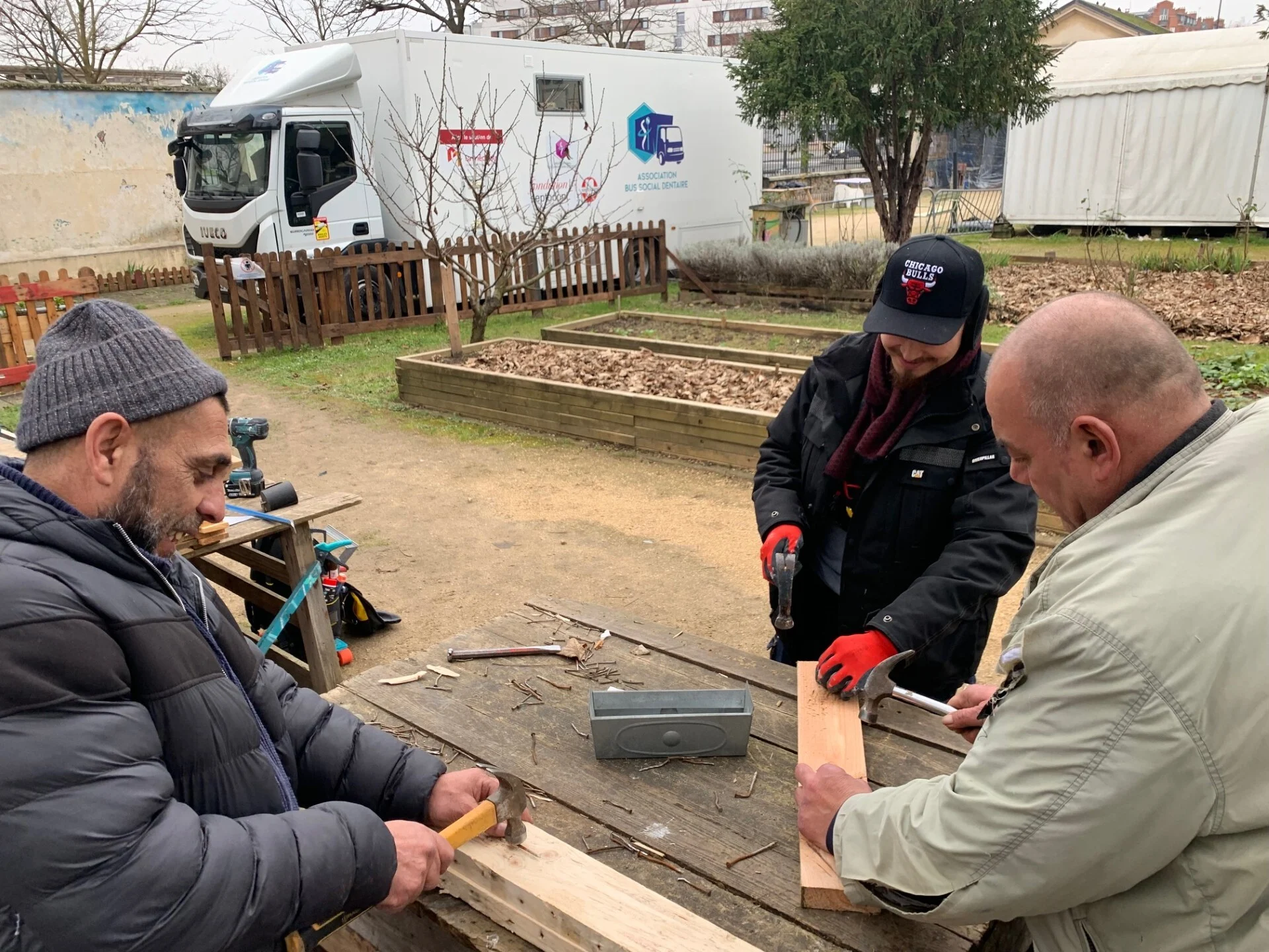 Group of people doing woodwork on a bench in the park.