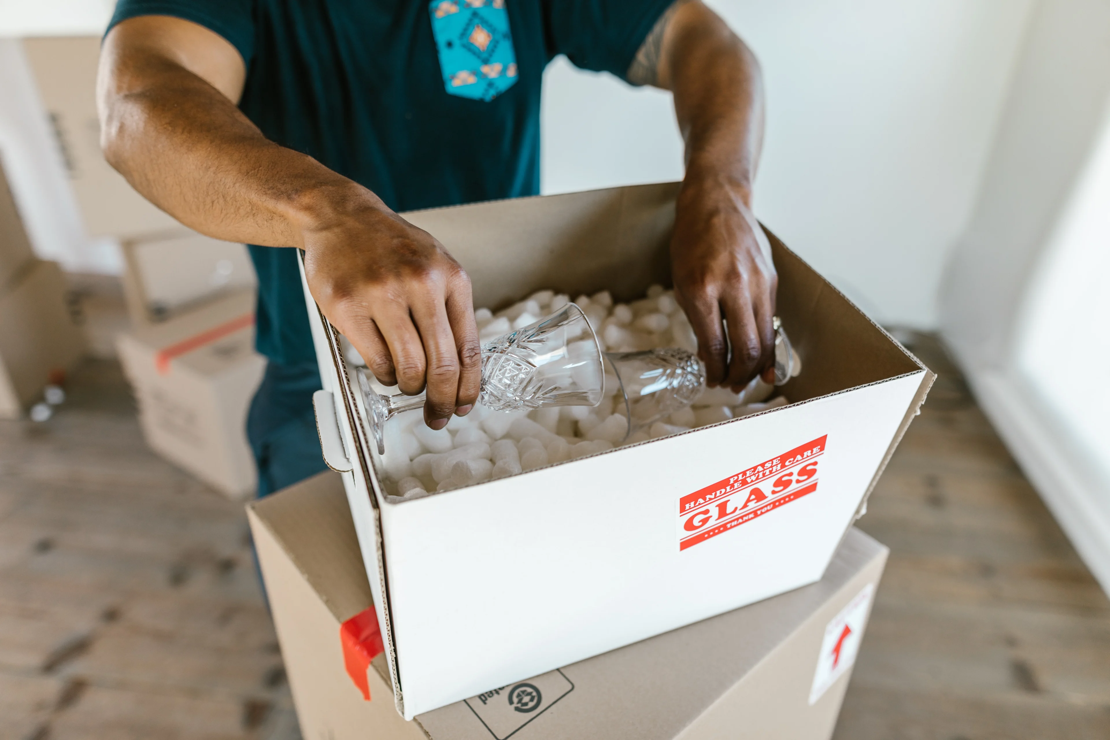 an image of a person placing glass dishes into a box with packing peanuts