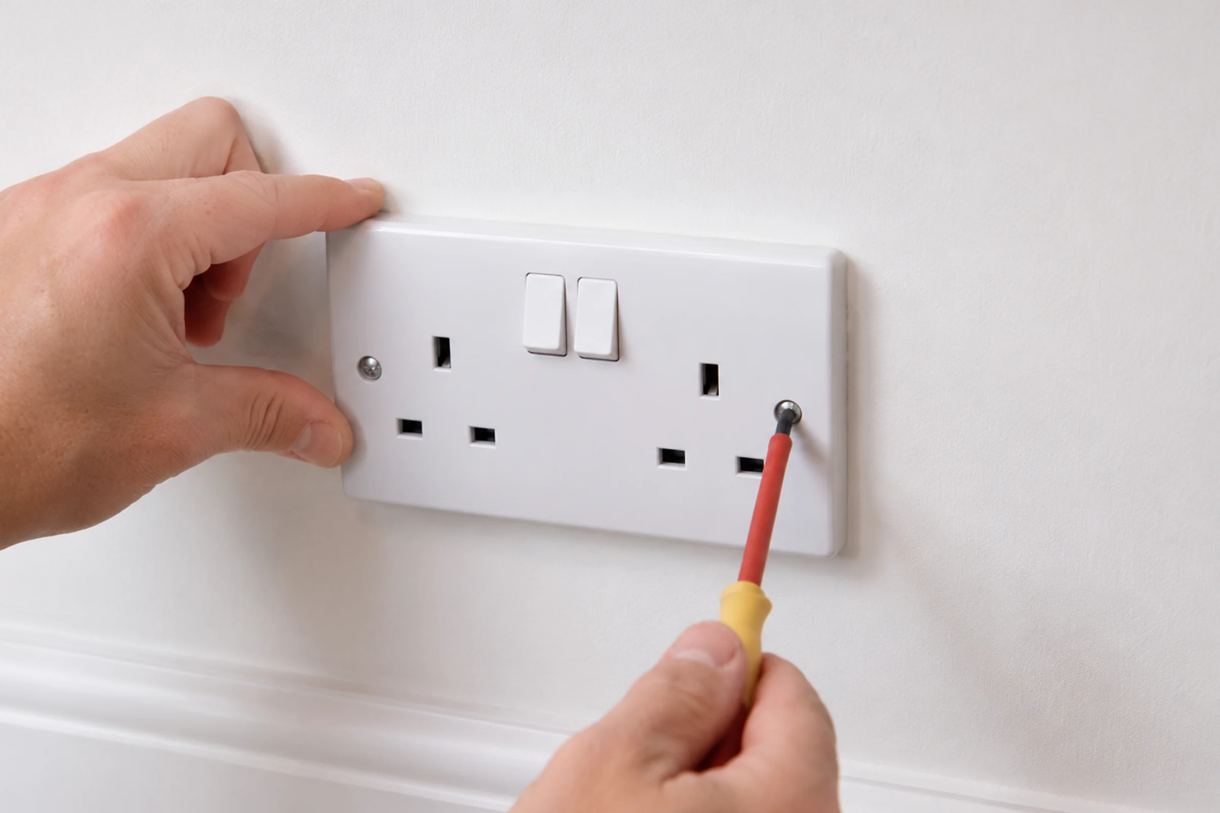 A person installing a switch next to an electrical socket with a drill. 